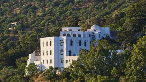 A white monastery with green windows, nestled in wooded hills under a clear sky, Monastery tis Apokalipsis, Patmos, Dodecanese, Greek Islands, Greece, Europe