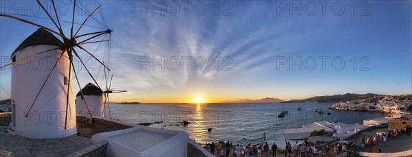 MYKONOS, GREECE, MAY 29, 2019: Panorama of traditional greek windmills on Mykonos island on sunset with dramatic sky and Little Venice quarter with tourist crowd