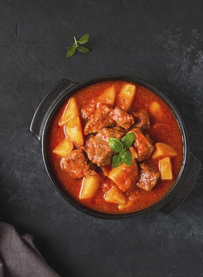 Stew with potatoes, in tomato sauce, with spices and herbs, close-up, no people, on a black background