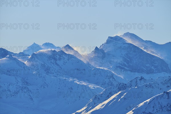 Snowy mountain peaks backlit with flying snow, against a clear blue sky in a wintry landscape, Leukerbad, Leuk, Valais, Switzerland, Europe
