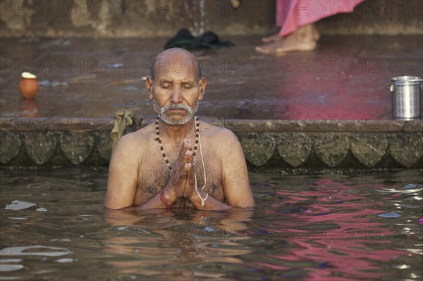 Indian man bathing and praying in the Ganges river at a ghat at Varanasi, Uttar Pradesh, India, Asia