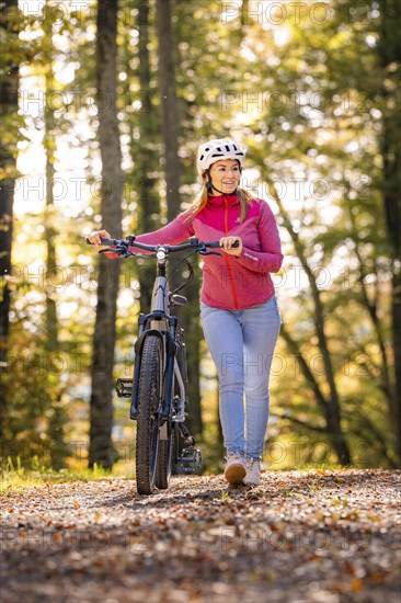 Woman pushing ebike through the autumn forest, Black Forest, Gechingen, Germany, Europe