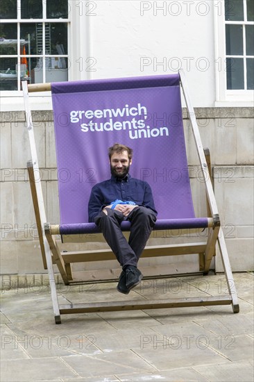 Young man sitting in giant deckchair outside the Students' Union, Greenwich, London SE10, England, UK