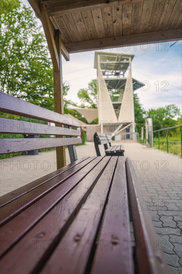 A wooden bench next to a hiking trail offers a view of a large modern observation tower, Rappbodetalsperre, Harz, Germany, Europe