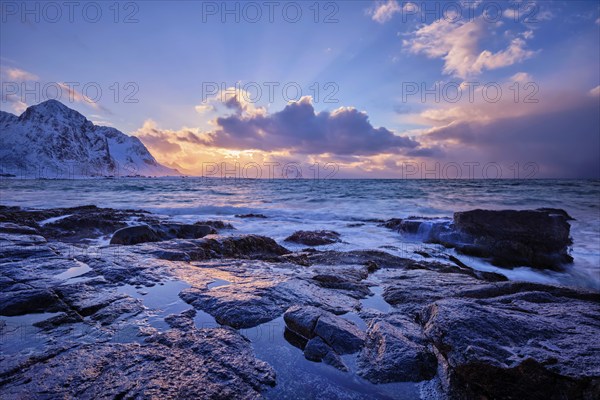 Waves of Norwegian sea on rocky coast in fjord on sunset with sun. Skagsanden beach, Lofoten islands, Norway, Europe