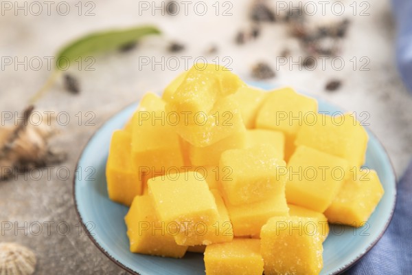 Dried and candied mango cubes on blue plate on brown concrete background and linen textile. Side view, close up, selective focus, vegan, vegetarian food concept