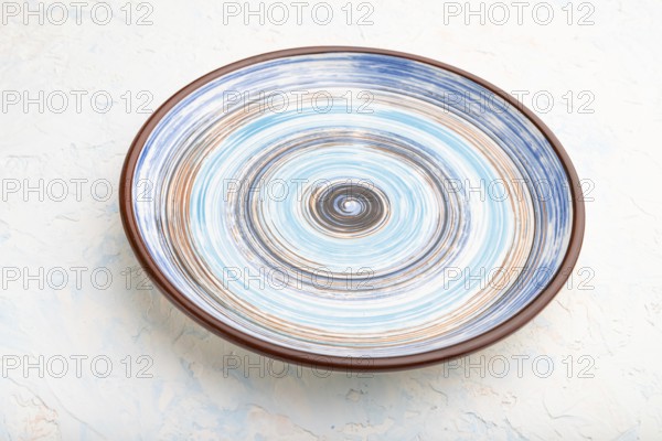 Empty blue ceramic plate on white concrete background. Side view, close up