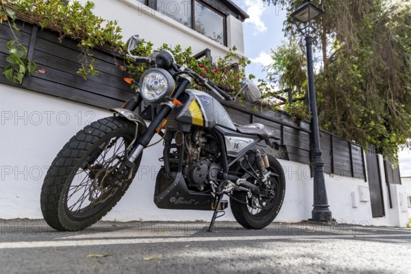 A stylish motorbike is parked on a street next to a house surrounded by green plants, Canary Islands, Lanzarote, Spain, Europe