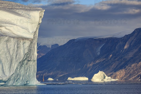 Sailing boat, ship in fjord in front of large icebergs and mountains, evening light, Scoresby Sound, East Greenland, Greenland, North America
