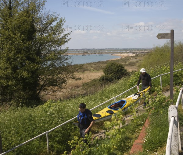 Two men carrying a canoe down to the beach, West Mersea, Mersea Island, Essex, England, United Kingdom, Europe