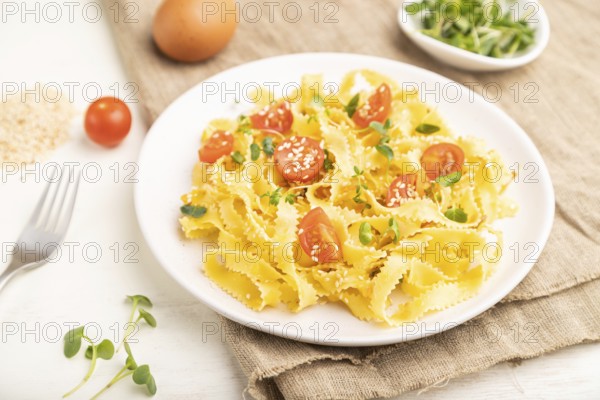 Reginelle semolina pasta with tomato, eggs, sesame and microgreen sprouts on a white wooden background and linen textile. Side view, close up, selective focus
