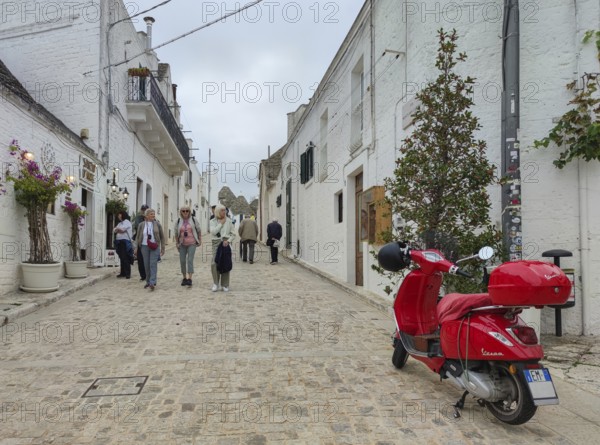 A picturesque street with white buildings, a red Vespa and people walking along, Alberobello, UNESCO World Heritage Site, Apulia, Italy, Europe