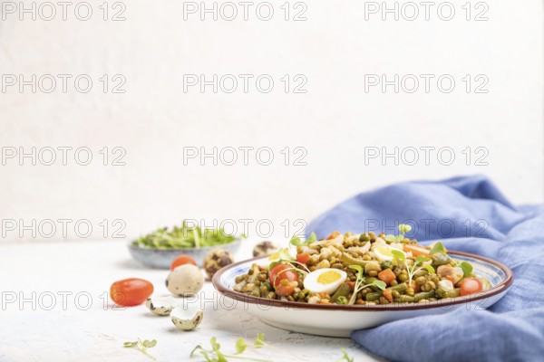 Mung bean porridge with quail eggs, tomatoes and microgreen sprouts on a white concrete background and blue textile. Side view, copy space, selective focus