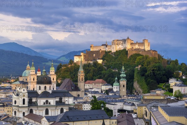 The illuminated Hohensalzburg Fortress towers above the city of Salzburg in the evening, surrounded by the Alps Salzburg, Salzburger Land, Austria, Europe