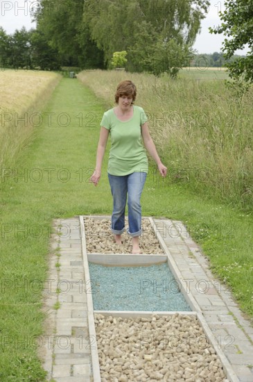 Woman walking barefoot over glass gravel and bottle corks, barefoot path Tilbeck Abbey, Havixbeck, North Rhine-Westphalia, Germany, Europe