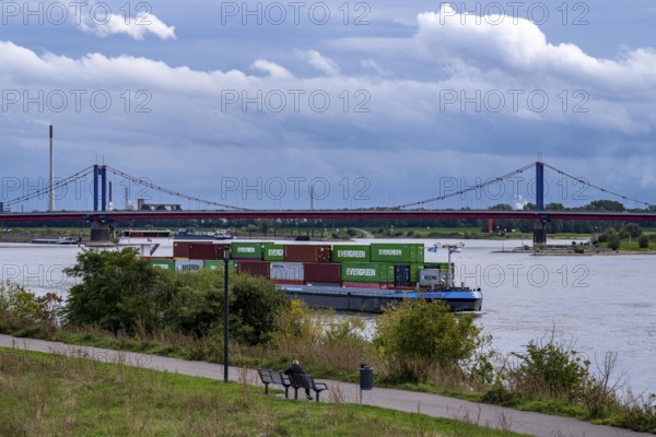 Cargo ship, loaded with containers, on the Rhine near Duisburg, the wheelhouse is raised to ensure a view over the containers to the bow, behind the Friedrich-Ebert-Bridge, riverside path on the Rhine dike near Duisburg Laar, North Rhine-Westphalia, Germany, Europe