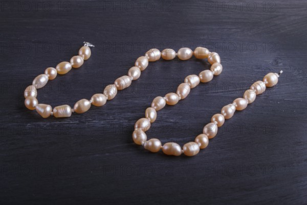 Caramel colored pearl beads on a black background. top view, close up