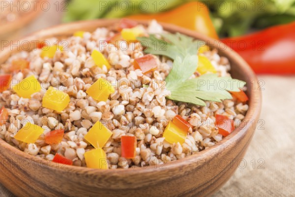 Buckwheat porridge with vegetables in wooden bowl on a white wooden background and linen textile. Side view, close up, selective focus, macro. Russian traditional cuisine