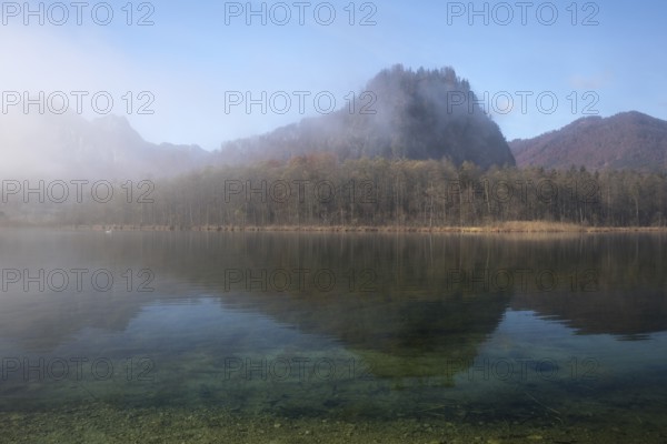 Lake Almsee in autumn with the mountain Ameisstein behind. The fog is lifting