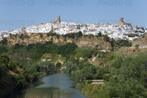 Whitewashed houses on a green hill along a river under a clear sky, Arcos de la Frontera, Guadalete river, Cadiz province, Cadiz, Andalusia, Spain, Europe