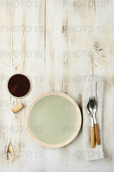 A minimalistic dining arrangement showcases a pale green plate next to a cup of dark beverage, complemented by a fork and knife on a linen napkin against a rustic wooden background