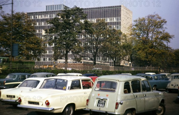 Cars in a car park next to a large modern office building, Great Britain 1966, location unknown