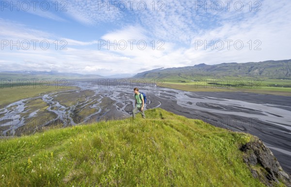 Hiker, young man on a hill, view over alluvial land, meandering river, Dímonarhellir, Suðurland, Iceland, Europe