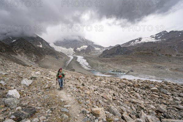 Mountaineer in bare stony mountain landscape, view of glacier Glacier de Cheilon and mountain peak Mont Blanc de Cheilon, with dark clouds, Valais, Western Alps Switzerland