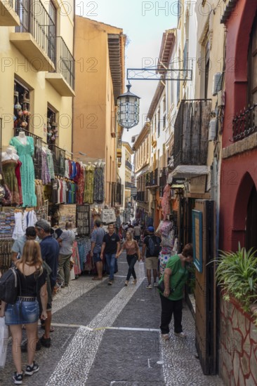 Lively market alleyway with lots of people and colourful items of clothing for sale, Granada