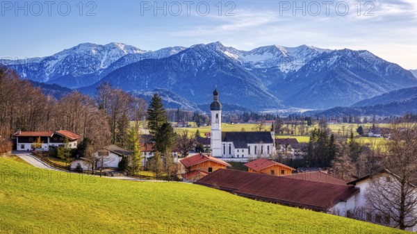 Bavarian village with church and red roofs, surrounded by green meadows and snow-covered Alps, Elbach