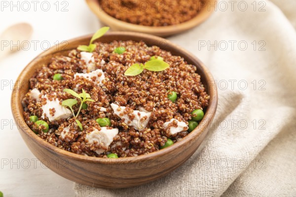 Quinoa porridge with green pea and chicken in wooden bowl on a white wooden background and linen textile. Side view, close up, selective focus