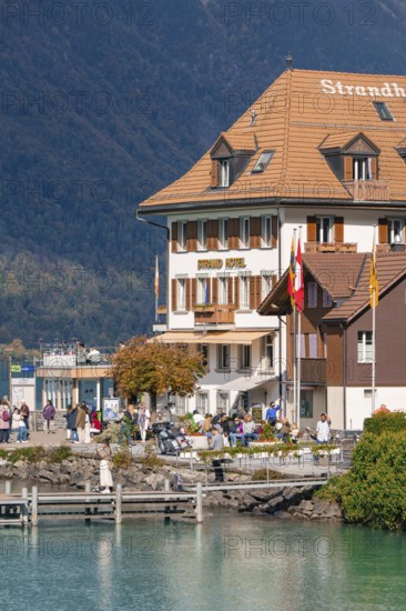 Beach hotel on the shore with people, mountains and autumn landscape in the background, Lake Brienz, Switzerland, Europe
