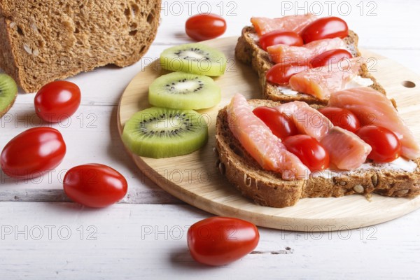 Smoked salmon sandwiches with butter and cherry tomatoes on white wooden background. close up