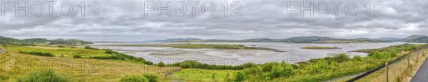 Wide landscape with river and green hills under a cloudy sky, panoramic view, Gweebarray Bay