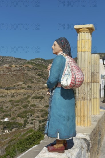 Wooden statue of a woman in traditional dress in front of a mountainous landscape, Olymbos, Karpathos, Greece, Europe
