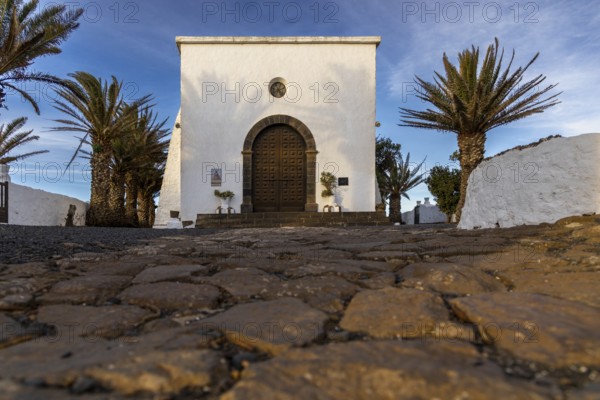 White chapel with palm trees and cobblestones in the foreground under a blue sky, Canary Islands, Lanzarote, Spain, Europe