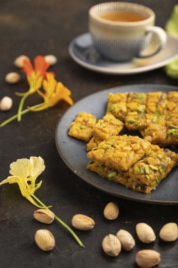 Traditional iranian dessert sohan with cup of green tea on a black concrete background and green textile. side view, close up, selective focus