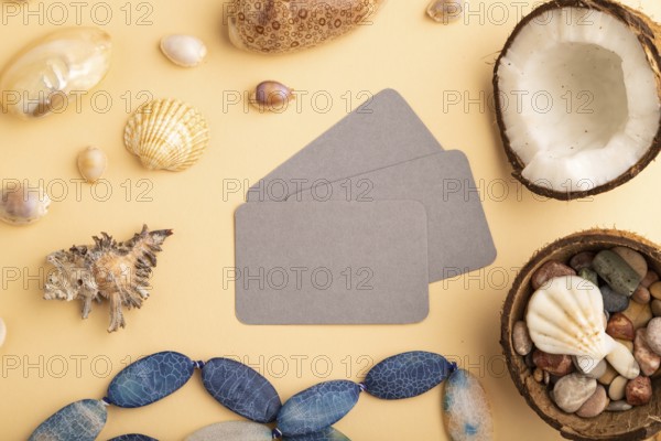 Brown paper business card with coconut, seashells, pebbles, beads on orange pastel background. Top view, flat lay, copy space. Tropical, healthy food, vacation, holidays concept