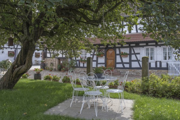 Idyllic garden with white iron furniture and half-timbered house in the background, Hunspach, Alsace, France, Europe