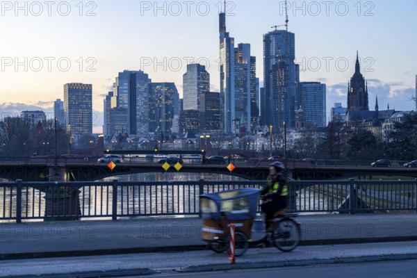 Skyline of the city centre of Frankfurt am Main, cargo bike cyclist on the rafter bridge, dusk, river Main, winter, Hesse, Germany, Europe