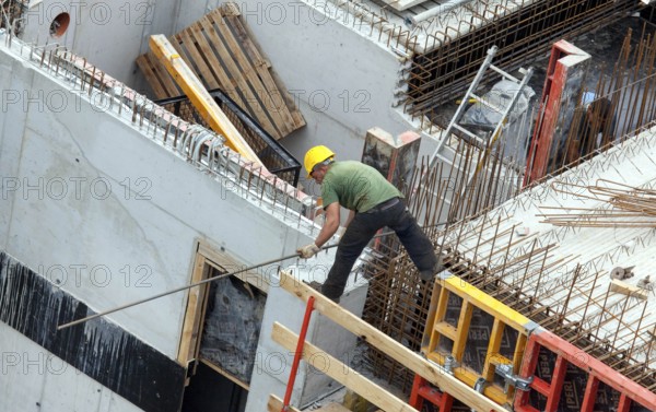 A construction worker juggles with an iron bar in his hand on a building site at lofty heights, Berlin, 18/08/2016