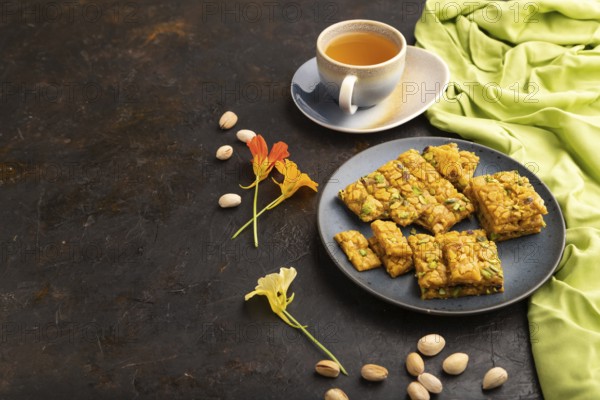Traditional iranian dessert sohan with cup of green tea on a black concrete background and green textile. side view, copy space