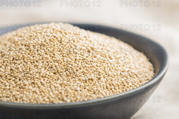 Blue ceramic bowl with raw white quinoa seeds on a gray concrete background and linen textile. Side view, close up, selective focus