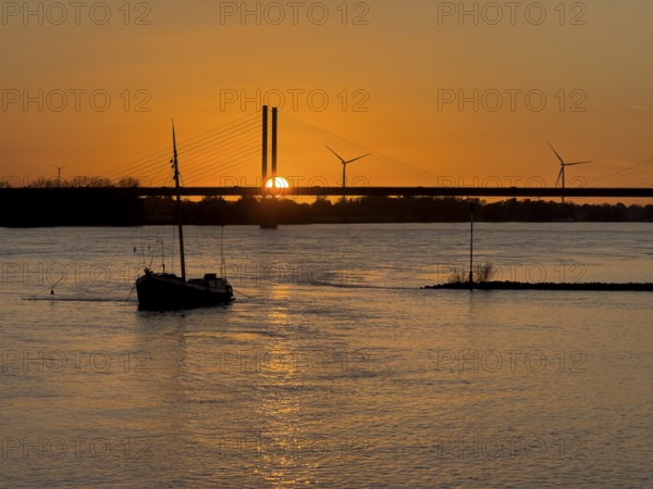 Sunset over river Rhine Lower Rhine, on the left in the foreground anchored historical ship Aalschokker fishing vessel, in the background west bank of Rhine and part of bridge Rhine bridge two-legged cable-stayed bridge, Rees, North Rhine-Westphalia, Germany, Europe