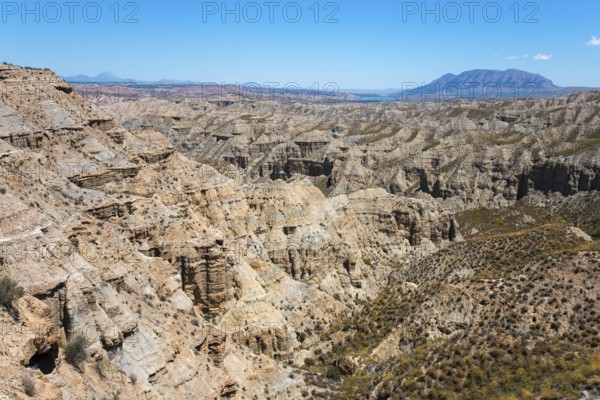 Large canyon area with rock formations and bare vegetation under a bright blue sky, Barranco de la Rambla del Pollo, Gorafe desert, Granada, Andalusia, Spain, Europe