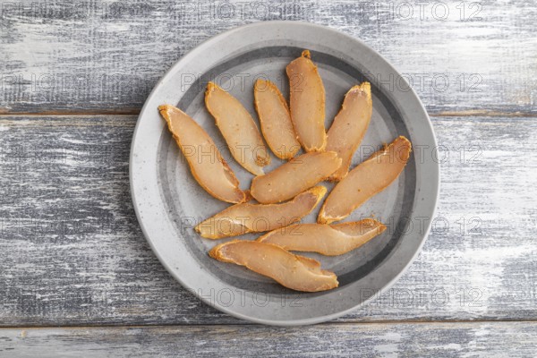 Salted meat on a wooden plate on a gray wooden background. Top view, flat lay, close up