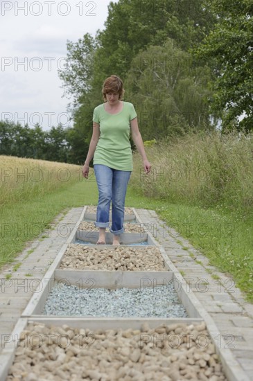 Woman walking barefoot over glass gravel and bottle corks, barefoot path Tilbeck Abbey, Havixbeck, North Rhine-Westphalia, Germany, Europe