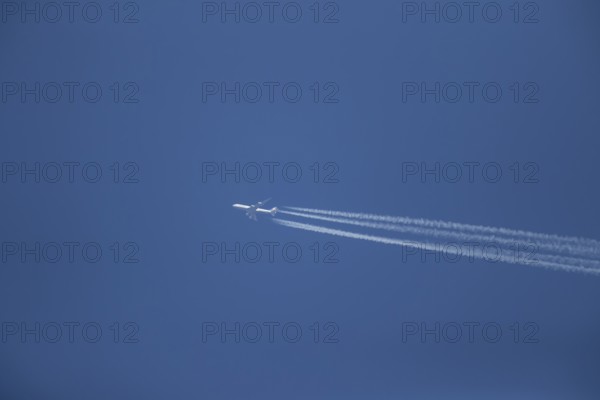Boeing 747 aircraft of Lufthansa airlines flying across a blue sky leaving a contrail or vapor trail in the atmosphere behind the plane, England, United Kingdom, Europe