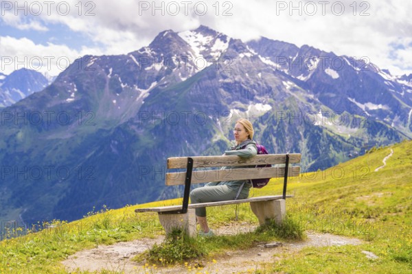A woman sits on a bench with a view of the snow-covered mountains and the hiking trail, Penken, Zillertal, Austria, Europe