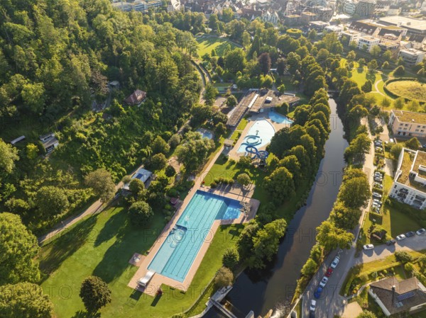 Spacious view of an outdoor swimming pool in the middle of a park, adjacent to a narrow river and urban infrastructure, Nagold, Black Forest, Germany, Europe